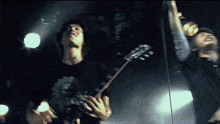 a man playing a guitar in a dark room with the letter d on the bottom right