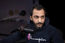 a man wearing a champion sweatshirt is standing in front of a microphone