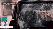 a man is sitting in a car with a broken windshield and is looking out the window .