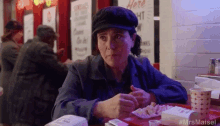 a woman in a hat is sitting at a table in a restaurant eating a sandwich .