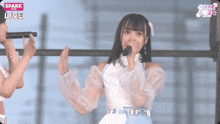 a girl singing into a microphone in front of a sign that says " spark live "