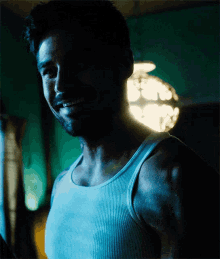 a man wearing a white tank top is smiling in a dark room