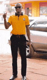 a man in a yellow shirt and black pants stands in front of a silver car