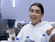 a woman in a white hoodie holds a blue cup