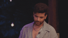 a man with a beard wearing a pearl necklace looks at the camera