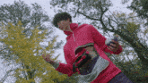 a man in a red hoodie is standing in a park with trees in the background
