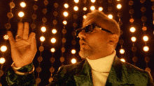 a man wearing sunglasses and a white turtleneck is dancing in front of a wall of lights