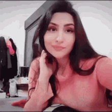a woman in a pink sweater is sitting on a bed and taking a selfie .