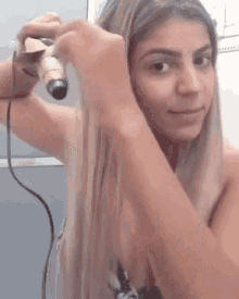 a woman is using a curling iron on her blonde hair