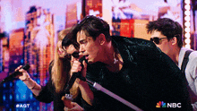 a group of people singing into microphones with a nbc logo in the corner