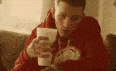 a man in a red hoodie holds a white cup in his hand