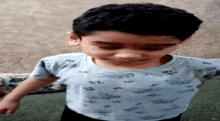 a young boy wearing a light blue t-shirt with cars on it is standing in front of a wall .