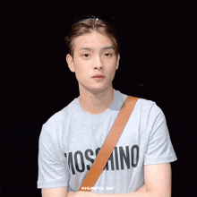 a man wearing a moschino shirt with a brown strap