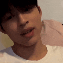 a close up of a young man 's face with his mouth open and a white shirt on .