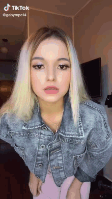 a woman is wearing a denim jacket and pink pants and has a tiktok account behind her