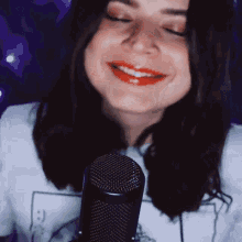 a woman is smiling in front of a microphone with a smiley face on her shirt