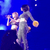 a woman singing into a microphone while another woman holds a drum on stage