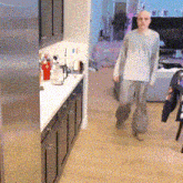 a man walking in a kitchen with a stainless steel refrigerator in the background