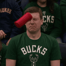 a man wearing a green bucks shirt holds a red cup to his eye