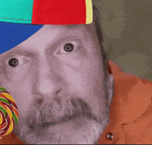 a man wearing a colorful hat is holding a colorful lollipop in front of his face