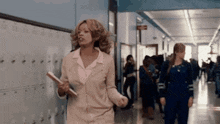 a woman is walking down a hallway holding a book and a clipboard .