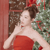a woman in a red dress with a pearl necklace is standing in front of a christmas tree