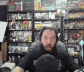 a man with a beard is sitting in front of a microphone in a room full of toys