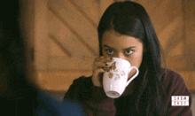 a woman is drinking from a white mug with a butterfly on it
