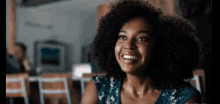 a woman with curly hair is smiling at the camera while sitting at a table in a restaurant .