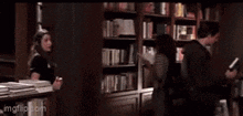 a man and a woman are standing in a library looking at books .