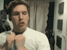 a man in a white shirt is tying his tie in a room .