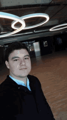 a man in a black jacket stands in a dark room with a picture of a man on the wall