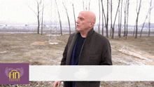 a man stands in a field with trees in the background and a purple banner with the letters ht