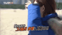 a woman in a blue jacket is standing on a beach with korean writing on the bottom