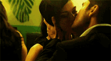 a man and a woman are kissing in front of a wall with a leaf on it