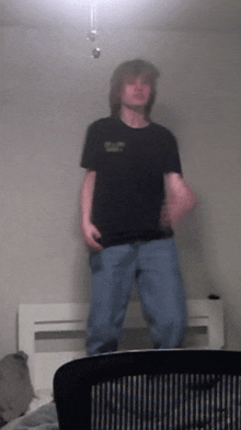 a man wearing a black shirt that says ' army ' on it stands in front of a bed