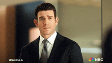 a man in a suit and tie is standing in front of a nbc sign