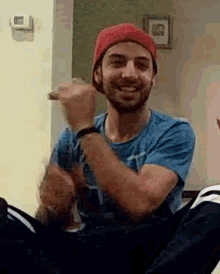 a man wearing a red hat and a blue shirt is sitting on a couch and smiling .