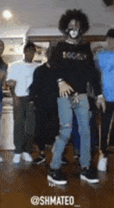 a man with a mask on his face is dancing in a room with other people .