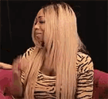 a woman with long blonde hair is sitting on a couch wearing a zebra print shirt .