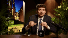 a man in a suit and tie sitting in front of a microphone with a mug that says af