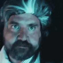 a man with a beard and a wig on his head looks at the camera .