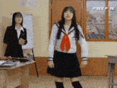 a girl in a school uniform is dancing in a classroom while another girl stands in the background .