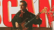 a man is playing a guitar in front of a large red sign that says can