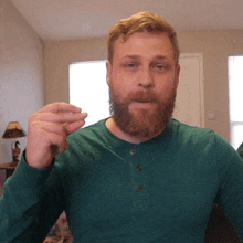 a man with a beard wearing a green shirt is making a hand gesture