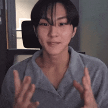 a man in a grey shirt is making a gesture with his hands