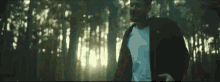 a man is walking through a forest with trees in the background .