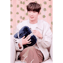 a young man sitting on a couch holding a blue pillow with a straw in his hand