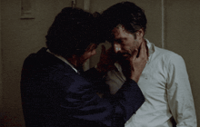 a man in a suit and tie touches another man 's neck