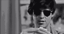 a man wearing sunglasses is holding a piece of paper in his hand .